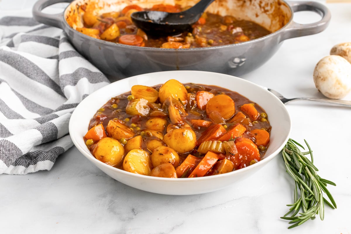 white bowl of old-fashioned vegan stew sitting in front of a gray cooking pot